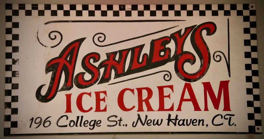A vintage Ashley’s Ice Cream sign with red script lettering and a checkered border reading 196 College St., New Haven, Ct.