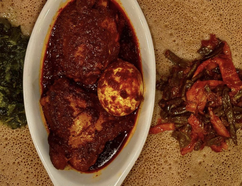Lalibela’s doro wat, chicken in a deep red berbere sauce in an oval dish set on injera beside vegetable sides