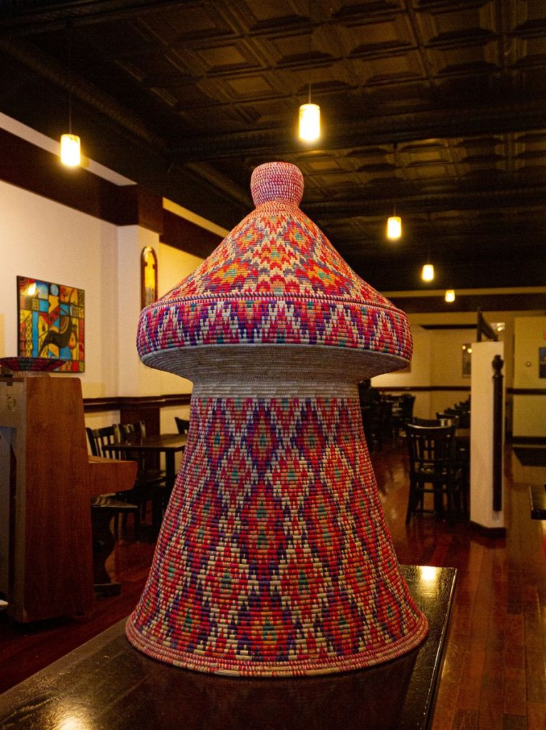 A tall woven mesob basket table in red, pink and blue patterns inside Lalibela’s dining room