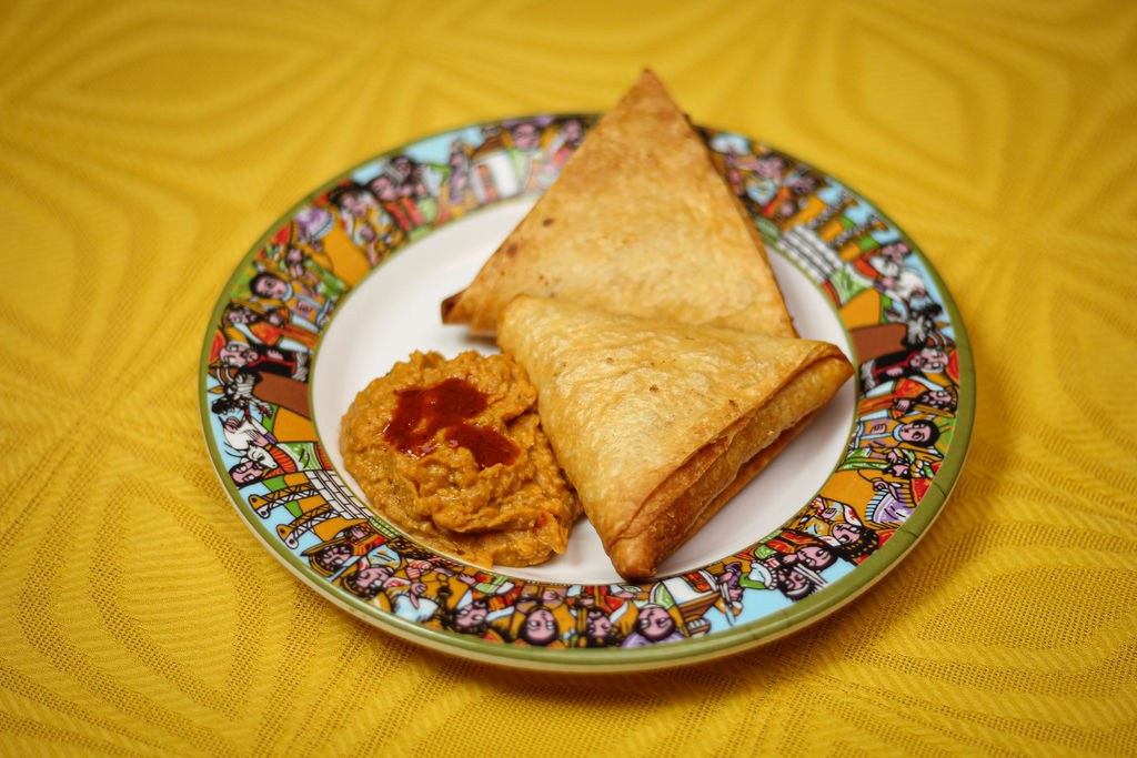 Two golden sambusa pastries on a patterned plate with a small mound of chickpea dip