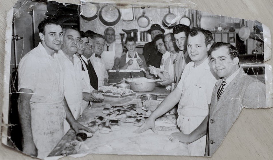 A vintage black-and-white photo of bakers and staff gathered behind a long work table at Lucibello’s