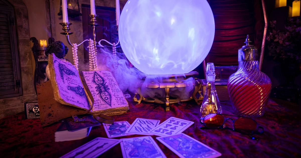 A candlelit table with a glowing crystal ball, tarot cards, an open spell book and potion bottles, from the Yale Peabody Museum’s Eternal Night Halloween promotion