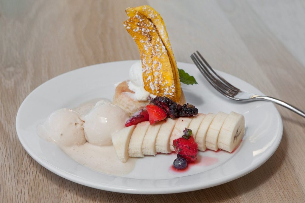Banana tres leches dessert with sliced banana and berries at Shell & Bones