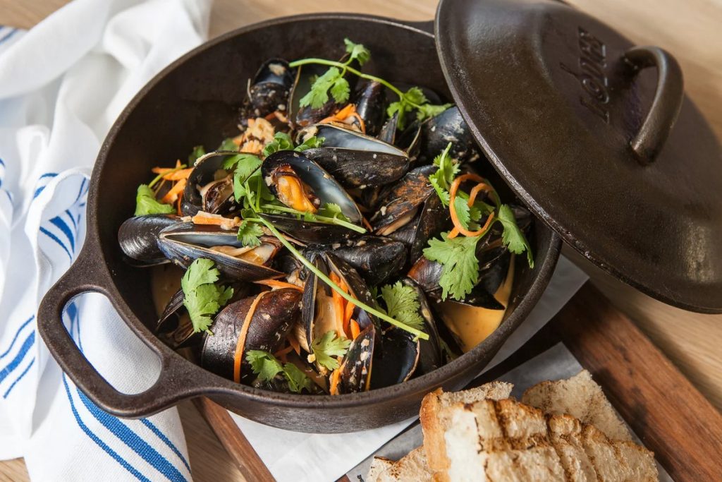 A black cast-iron pot of mussels with herbs and bread at Shell & Bones