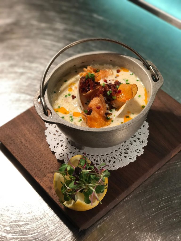 A pot of Shell & Bones New England clam chowder on a wooden board
