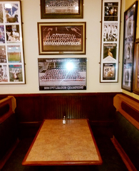 A wooden booth beneath framed Yale team photos at Yorkside Pizza