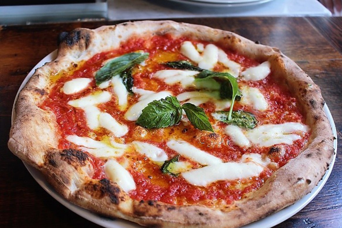 A Zeneli Margherita pizza on a white plate on a wooden table