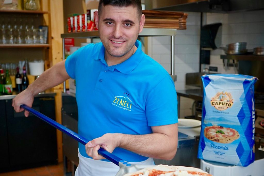 A Zeneli pizzaiolo with a Caputo flour bag and a pizza on a peel